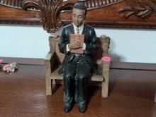 (BR1) YOUNG BRAND PREACHER SITTING ON A BENCH WITH A BIBLE FIGURINE. IT MEASURES 5-1/2"W X 4-1/2"D X
